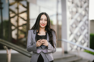 Confident businesswoman standing outdoors in business attire with smartphone, reflecting ambition,...