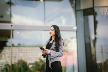 Confident businesswoman standing outdoors in business attire with smartphone, reflecting ambition,...