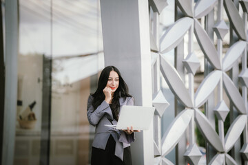 Confident, determined businesswoman
Standing in front of a modern office building holding a laptop,...
