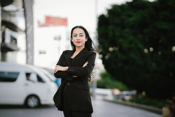 A confident, stylish woman in a black blazer walks through the city with coffee and smartphone in...