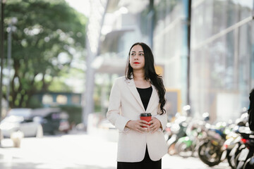 A businesswoman in a chic white blazer and holding a cup of coffee represents modern elegance,...