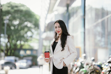 A businesswoman in a chic white blazer and holding a cup of coffee represents modern elegance,...