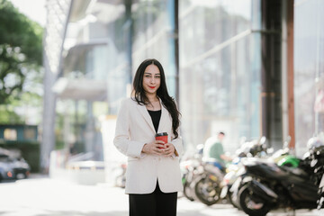 A businesswoman in a chic white blazer and holding a cup of coffee represents modern elegance,...