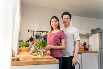 Portrait of Asian couple holding groceries on kitchen counter after shopping.