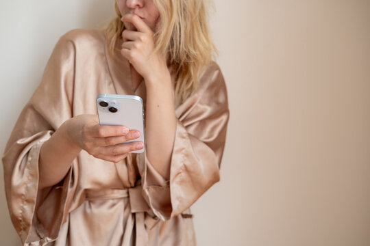 Woman wearing silk bathrobe scrolling a smartphone in bedroom or hotel room. Social media, dating app or internet browsing. Communication or networking.