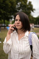 Vertical portrait of serious woman in blouse on phone in a busy street. Concept: urban contrast, inner focus, modern lifestyle, connection in motion.