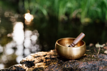 Tibetan singing bowl placed on a rock in the middle of a gently flowing river. Serene natural landscape with a calm atmosphere, symbolizing meditation, mindfulness and balance. Background for wellness