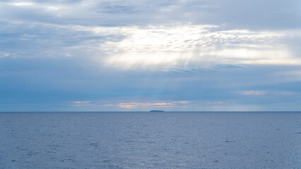 Distant island on the horizon with sun rays breaking through clouds over the ocean