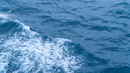 Rough blue ocean water with a prominent white wake and textured waves