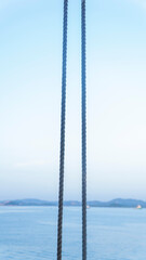 Two ropes hang vertically in front of a blue ocean and distant land