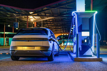 Electric vehicle charges at night near public bus station with illuminated charging infrastructure...