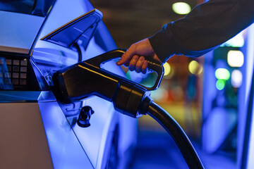 EV charging at night, close-up of hand plugging in electric car at charging station