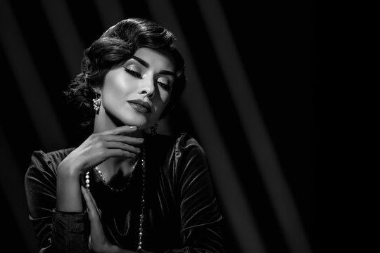 Black and white fashion portrait of elegant young woman with wavy hairstyle dressed in evening clothes. Retro girl in elegant black and white photo with vintage Hollywood hairstyle and actress charm