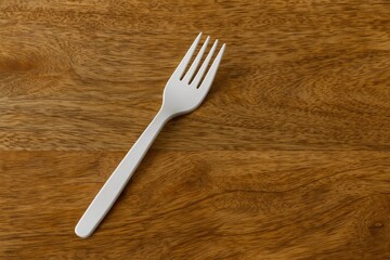 Disposable white plastic fork placed on a wooden table