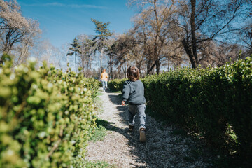 A little child strolls through a serene park, surrounded by neatly trimmed hedges and trees, enjoying the warm sunlight and nature's tranquility.