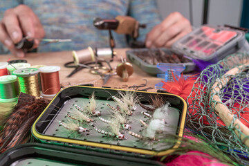 Man making trout flies. Fly tying equipment and material for fly fishing preparation .