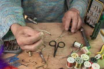 Man making trout flies. Fly tying equipment and material for fly fishing preparation .