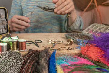Man making trout flies. Fly tying equipment and material for fly fishing preparation .