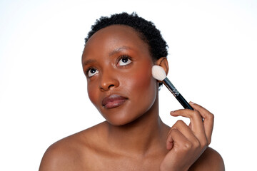 Woman applying cosmetic makeup with a brush in a bright studio setting to enhance her natural...