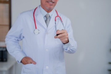 Senior male doctor wearing lab coat and stethoscope is holding a pen and smiling, suggesting a...