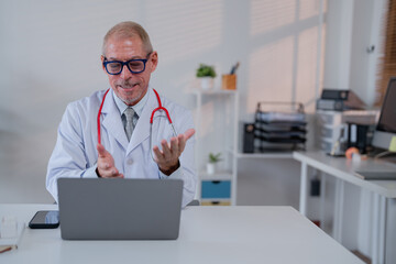Experienced doctor in white coat and glasses conducting a virtual consultation. He uses a laptop in...