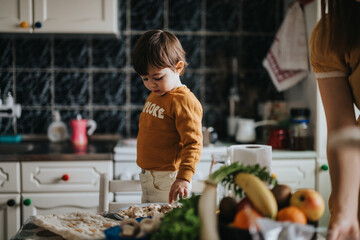 A curious young boy standing near a table in a kitchen, interacting with food items arranged on the surface within a cozy and casual environment