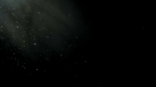 Floating white dust particles in light beam on black background