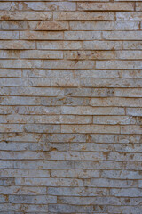Textured beige stone brick wall, close-up exterior surface captured in natural daylight
