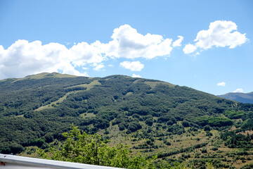 Expansive panoramic view of rolling green hills and forests under a clear sky, typical of the natural beauty found near Pescasseroli in Abruzzo, Italy.