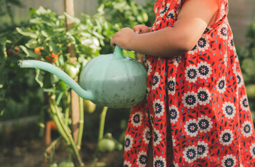 Child watering plants with a green watering can in a colorful dress