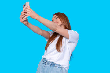 Young woman taking a selfie with a smartphone in front of a bright blue background at a casual...