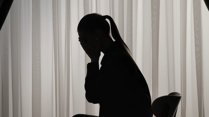 Silhouette of a distressed woman in front of backlit curtains