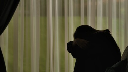 Silhouette of a distressed woman in front of backlit curtains