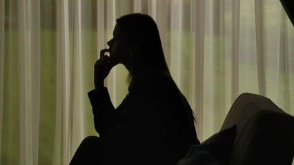 Silhouette of a distressed woman in front of backlit curtains