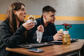 Two young people savor their meals indoors, displaying friendship and enjoyment in a comfortable setting.