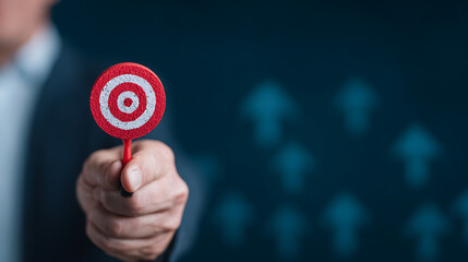 Businessman holding dartboard with red arrow hitting bullseye, symbolizing strategy and success on dark blue background with upward arrows concept. 61408837 1