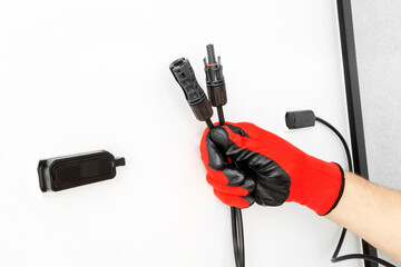 Close-up of technician's gloved hands connecting connectors of MC4 solar panels. Renewable energy concept.