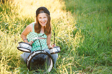 Beautiful smiling happy young little girl with long hair playing on the drums. Expressive Drummer Girl Playing Drums at Sunset. Rock Band Music Artist Learning a New Drum Solo