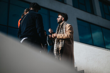 A group of young professionals engage in a discussion in an urban outdoor setting. They appear...