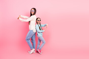Happy mother and daughter posing together wearing modern casual outfits against a cheerful pink background indoors