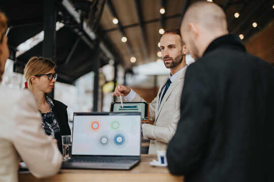 Businesspeople engaging in a meeting outdoors, discussing ideas and technology while collaborating around a laptop, showcasing teamwork, innovation, and professional interaction in an outdoor area.