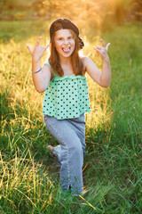 Portrait of attractive little girl smiling and looking at camera. Emotional portrait of happy little girl shows her tongue and fingers up at sunset. Smiling little girl. Childhood leisure concept