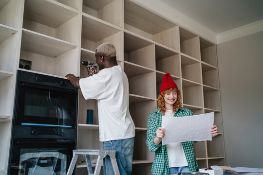 Smiling woman reading instruction manual near man using drill on rack at home