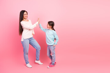 Mother and daughter sharing a joyful high-five in a casual setting on a vibrant pink background capturing a happy moment