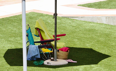 Tumbona vacía, sillas, toallas, chanclas, hierba y sombra en piscina de verano para el calor y el...