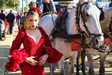 A beautiful woman dancing flamenco next to a white horse at the April fair in Seville, Spain. She...
