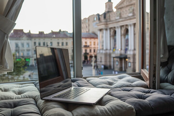 Cozy workspace with an open laptop by a window overlooking the historic Lviv Opera House and...