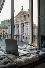 Cozy workspace with an open laptop by a window overlooking the historic Lviv Opera House and...