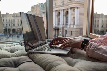 Hands typing on a laptop by a cozy window seat with a view of the historic Lviv Opera House in the...