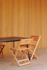 minimalist outdoor setting showcases wooden chairs and table against warm wood paneling, reflecting...